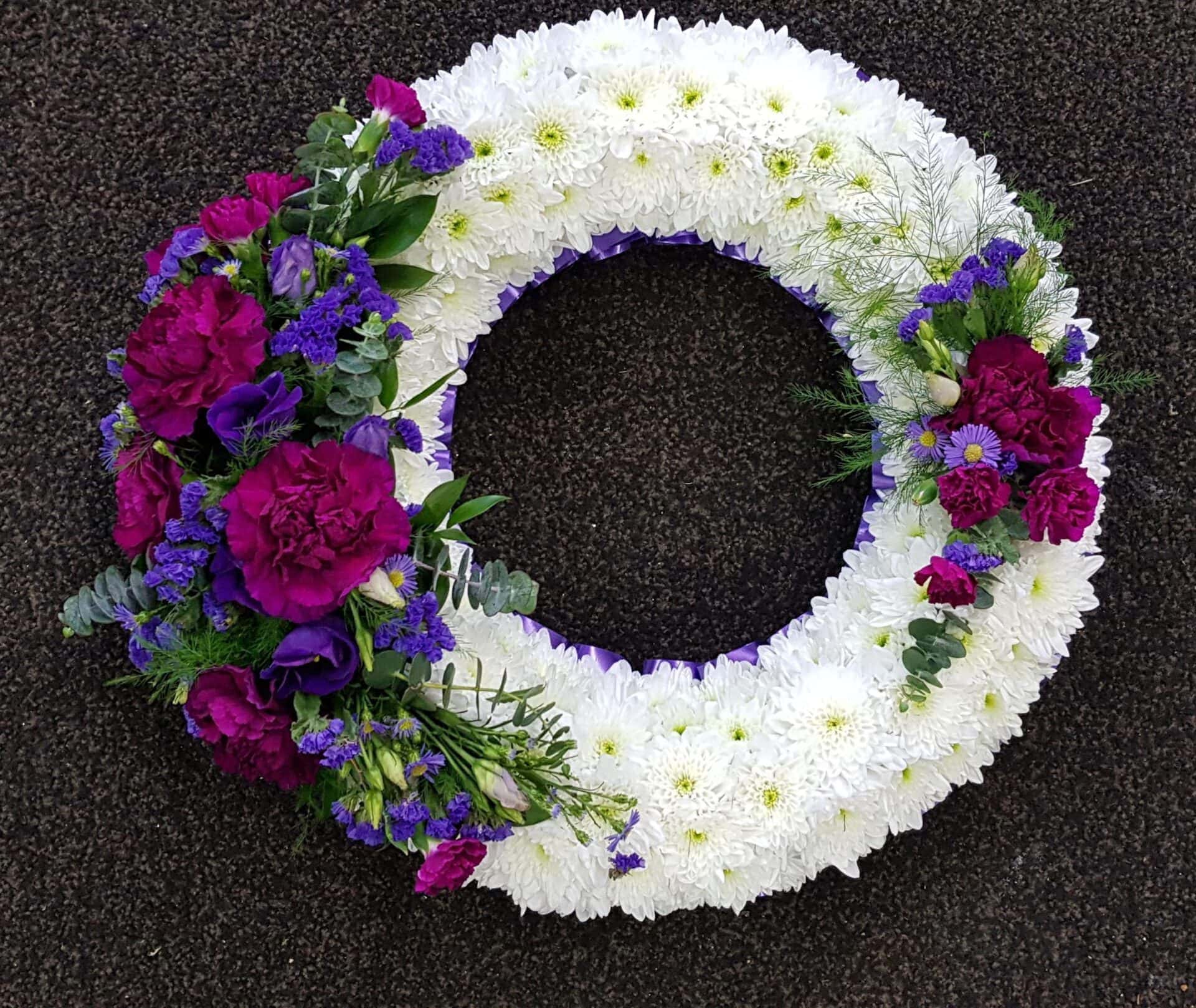 White based funeral wreath with purple ribbon edge and rich purple flower sprays