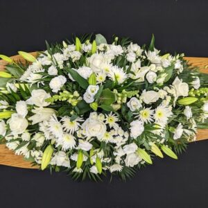 White coffin spray with roses and lilies on a wooden coffin