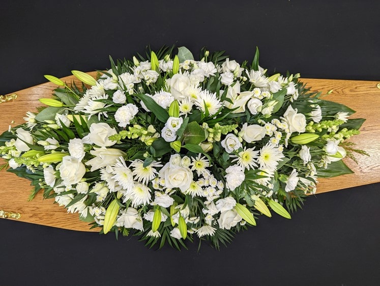 White coffin spray with roses and lilies on a wooden coffin