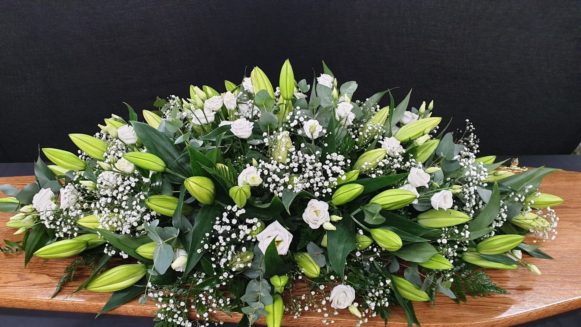 White lily and rose coffin spray with gypsophila on wooden coffin