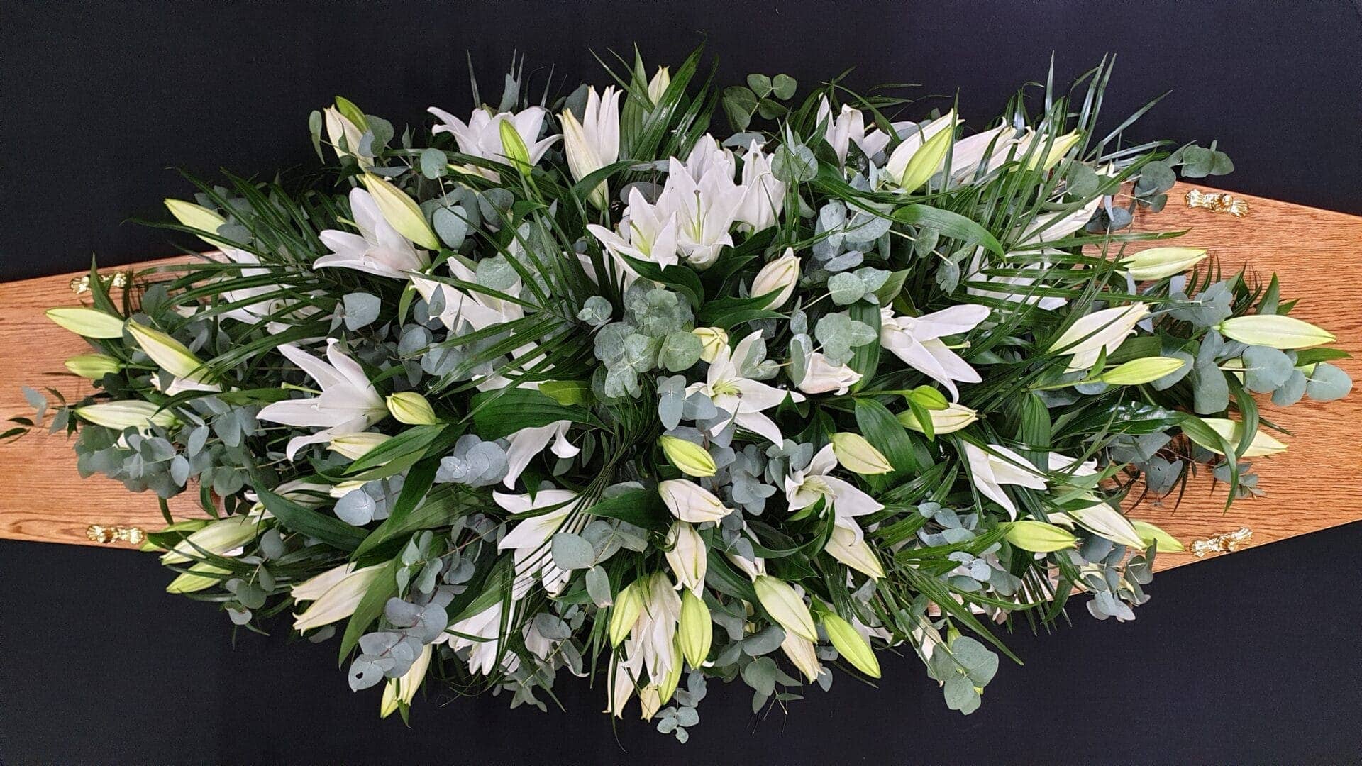 White lily coffin spray with eucalyptus on wooden coffin