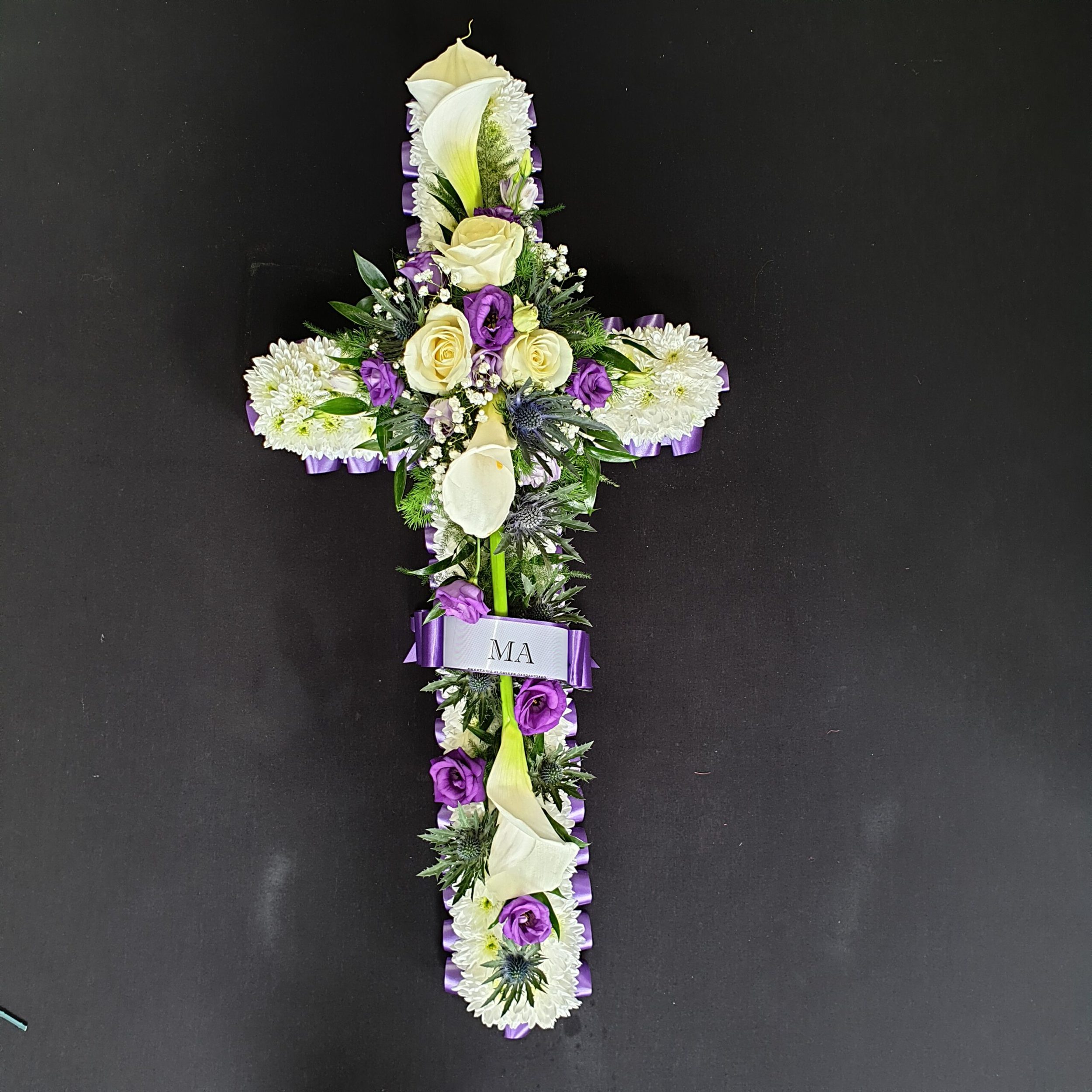 White and purple funeral cross with chrysanthemum base, roses, calla lilies and name ribbon