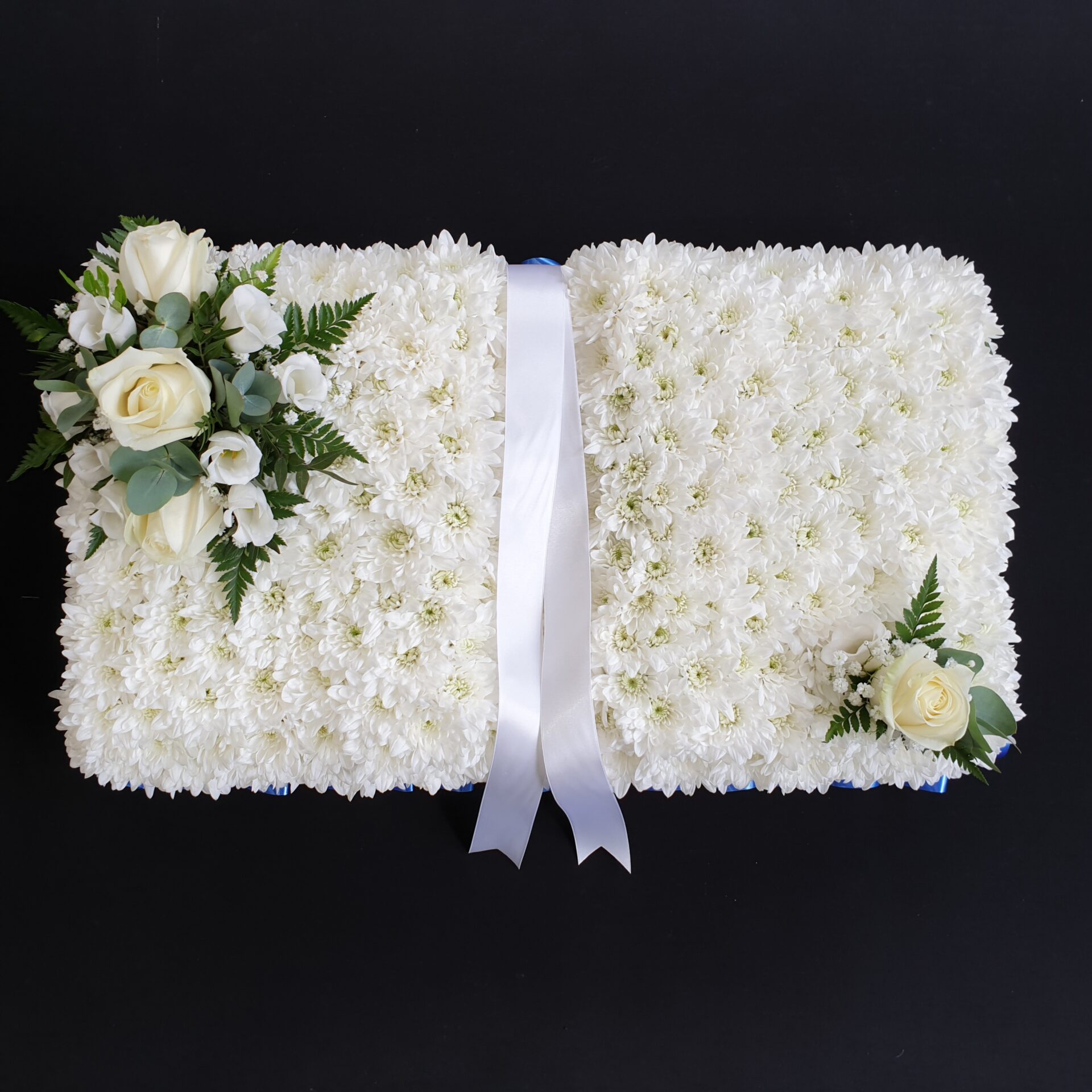 White rose funeral book tribute with massed chrysanthemum base and central white ribbon