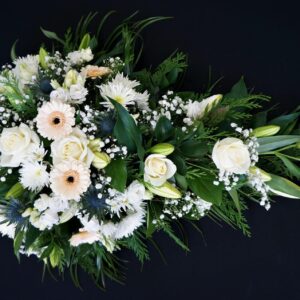 White rose and gerbera single ended funeral spray with lilies, gypsophila and greenery on a black background.