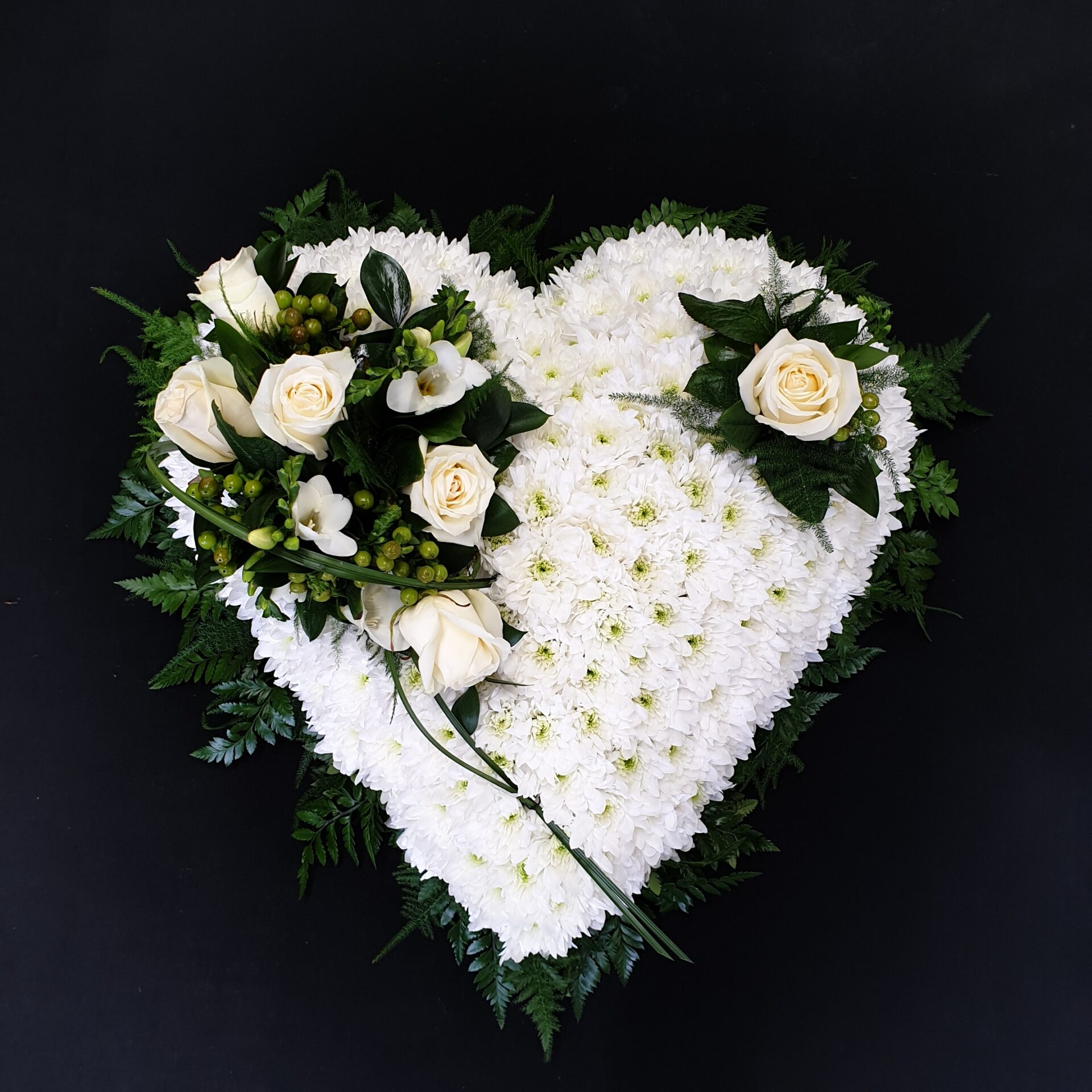 White chrysanthemum heart funeral tribute with ivory roses, berries and greenery on a black background