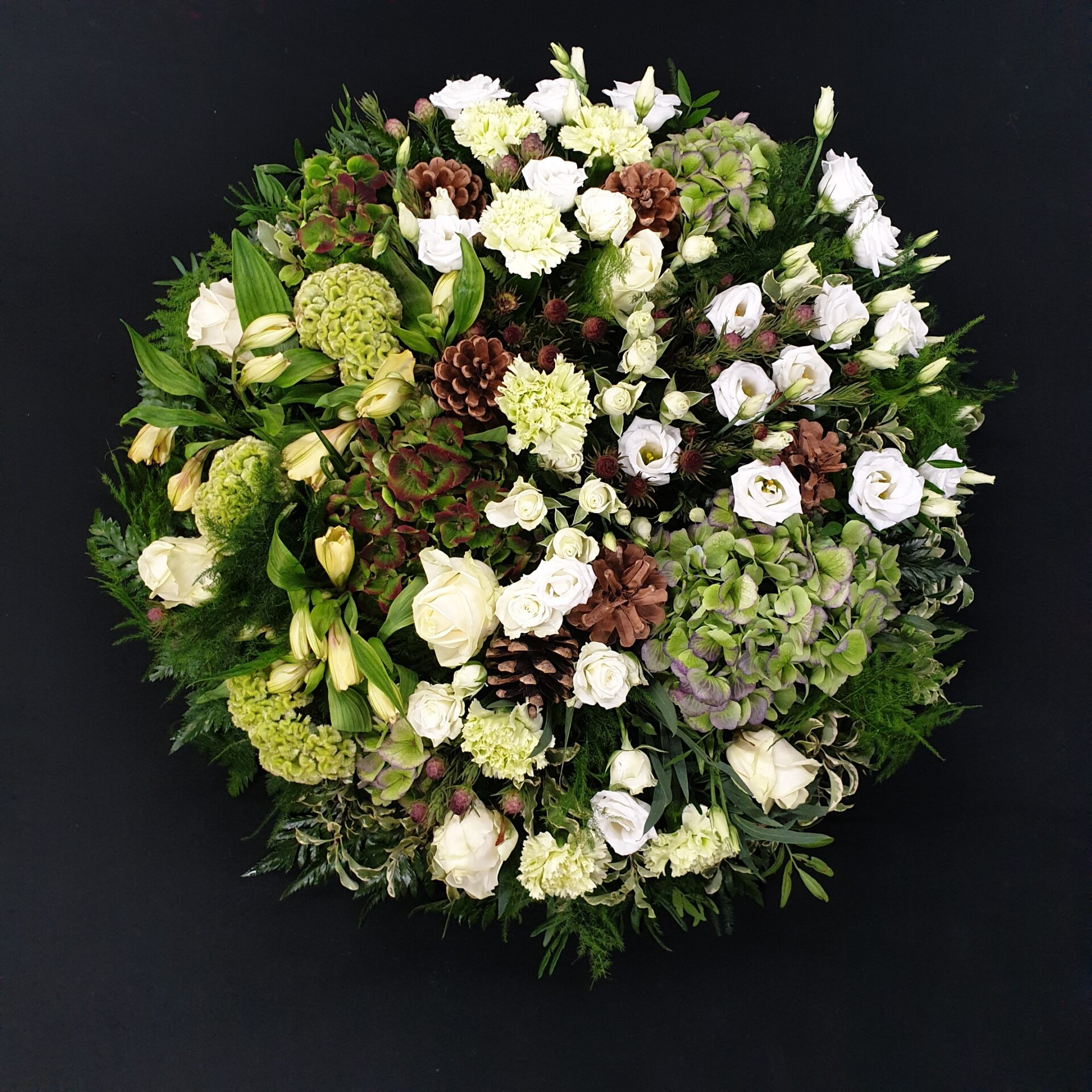 Woodland-style white and green funeral posy with roses, hydrangea and pine cones