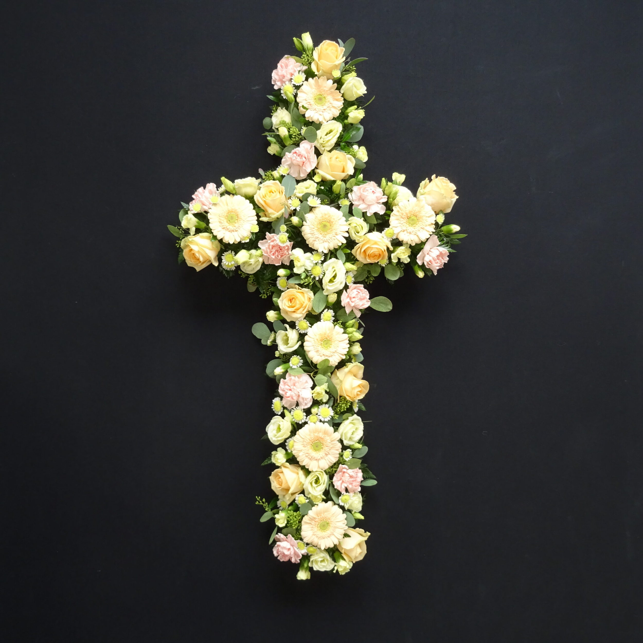 Soft yellow and peach flower funeral cross on black background