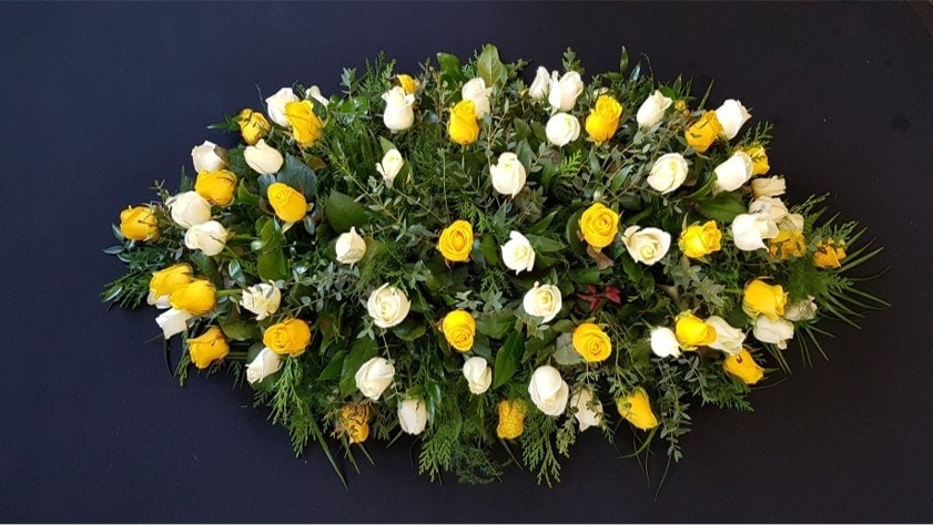 Yellow and white rose coffin spray with greenery on dark background