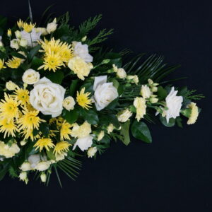 Yellow and white single ended funeral spray with roses, chrysanthemums, carnations and greenery on a black background.