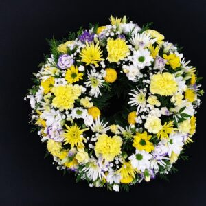 Yellow and white funeral wreath with carnations, daisy-style flowers, gypsophila and lilac accents